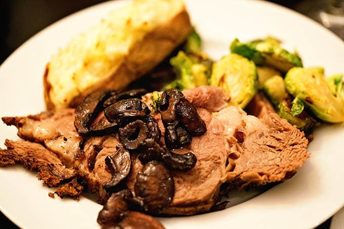 A white plate steak topped with mushrooms, twice baked potatoes and Brussels sprouts