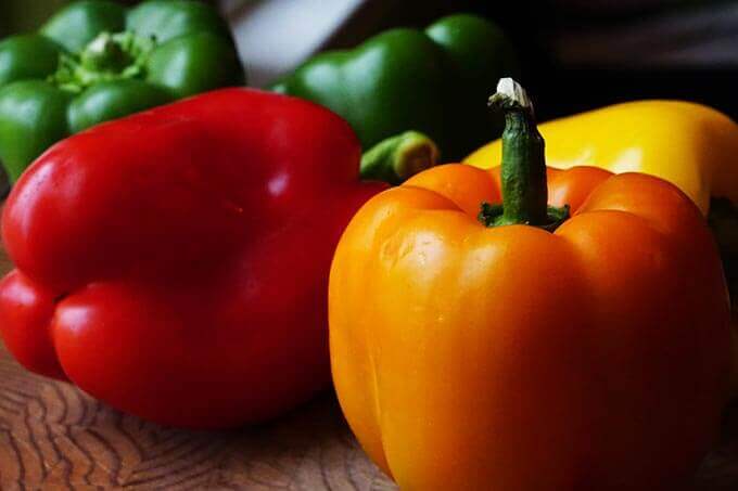 Red, green, orange and yellow bell peppers sitting on cutting board.