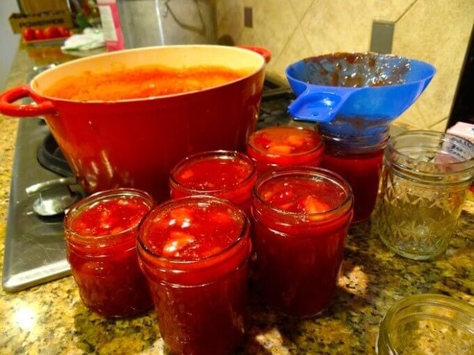 ladle the strawberry jam into jars.