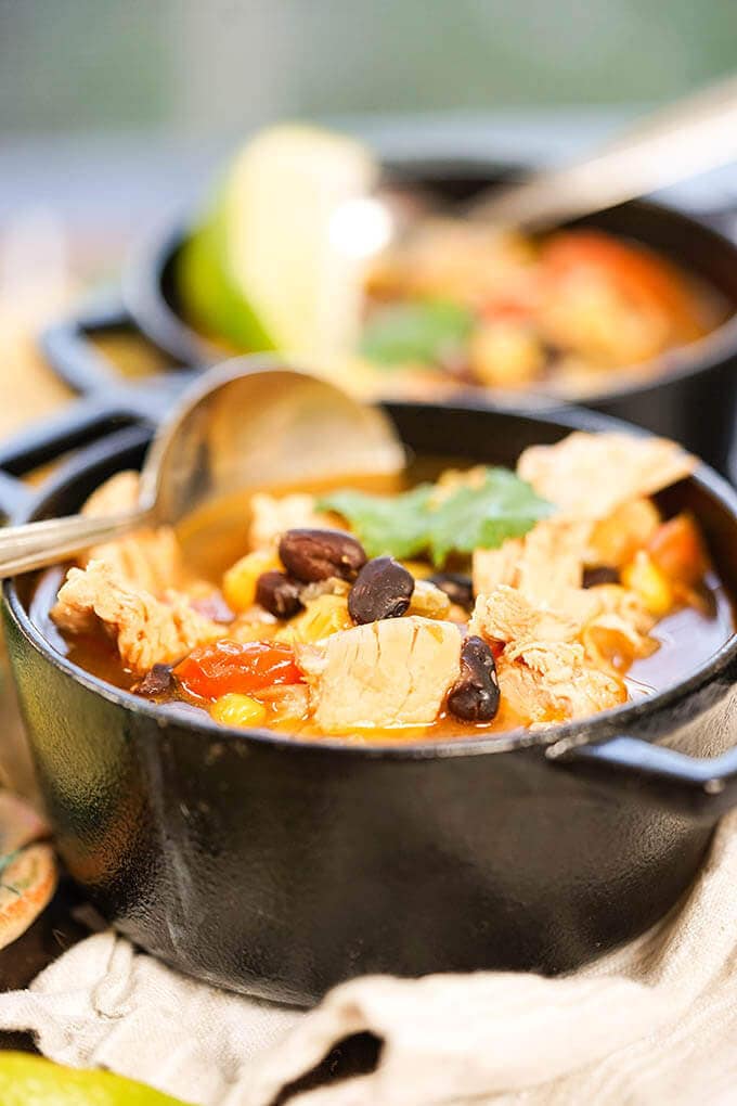 Crock Pot Chicken Taco Soup in black cast iron bowl with spoon.