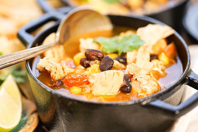Slow Cooker Chicken Taco Soup is a cast iron bowl with spoon.
