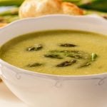 Vegetarian asparagus soup in white bowl serve with fresh homemade rolls.