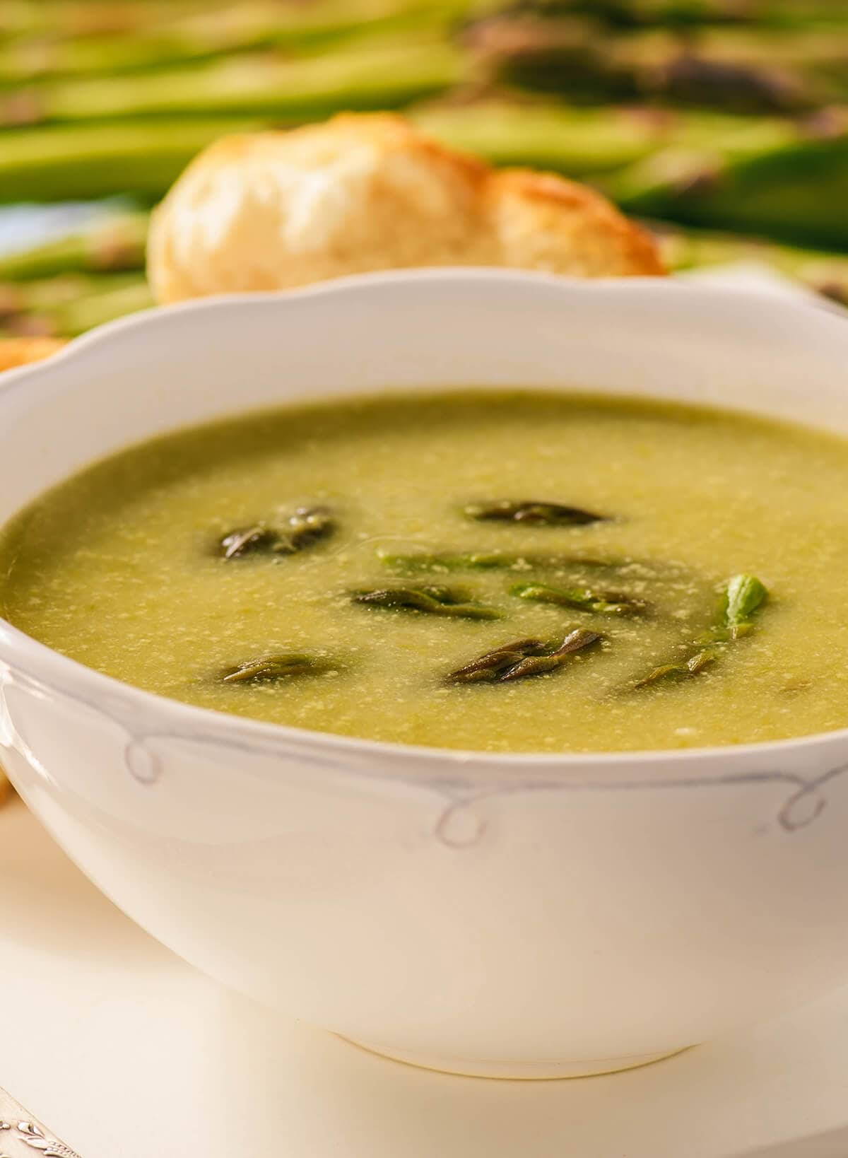 Vegetarian asparagus soup in white bowl serve with fresh homemade rolls.