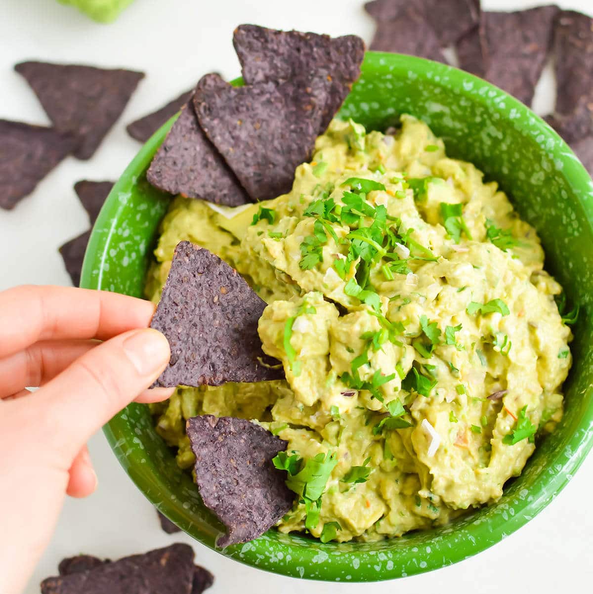 Dip in green bowl served with chips and with hand dipping a chip into the bowl.