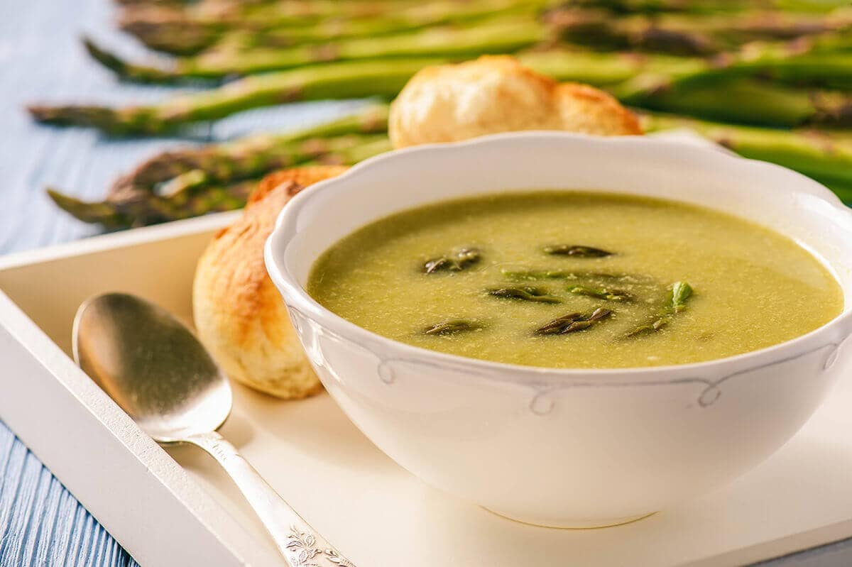 Soup on platter served with rolls and asparagus on the side.