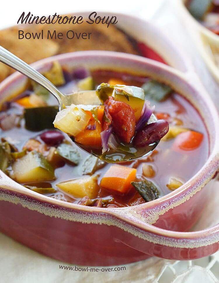 A spoonful of the best minestrone soup recipe. There's a red bowl in the background filled with more minestrone soup.