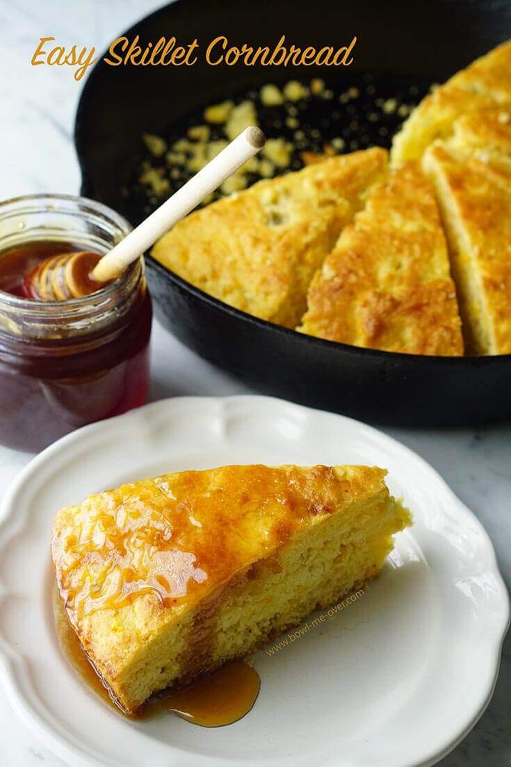 Sliced cornbread in a cast iron skillet with a wedge on white plate topped with melted butter and honey.