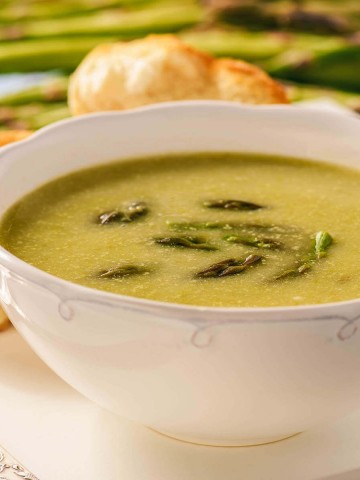 Creamy Soup in white bowl topped with asparagus spears.