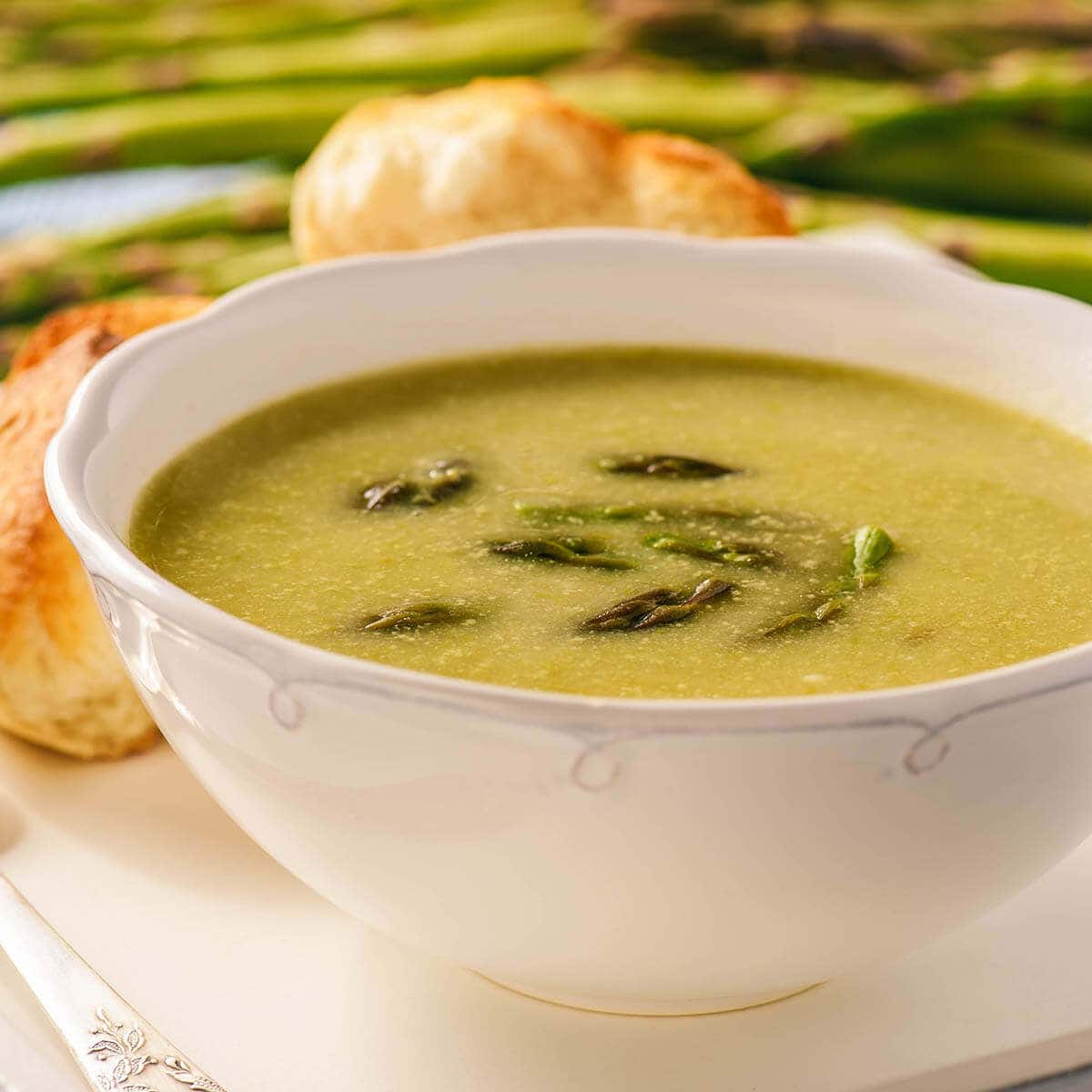 Creamy Soup in white bowl topped with asparagus spears.