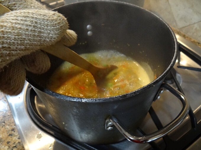 Pepper jam boiling on the stove being stirred with wooden spoon.