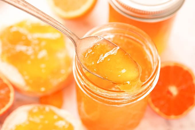 Orange jam in a pint jar with spoon. Bagels topped with fresh homemade jam.