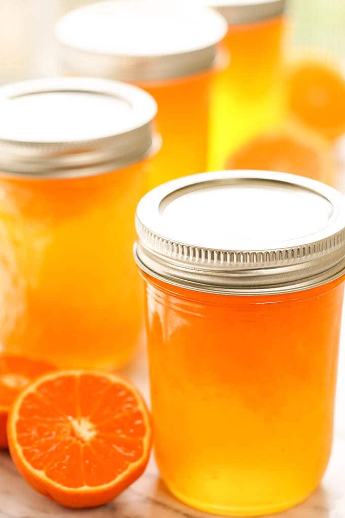 Four jars filled with mandarin orange jelly surrounded by wedges of mandarins