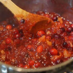 Cranberry sauce cooking in pan with wooden spoon.