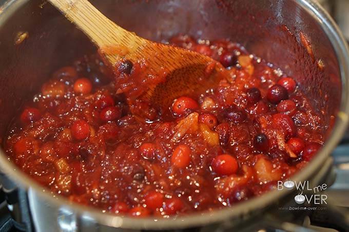 Cranberry Sauce cooking in pan being stirred with wooden spoon.
