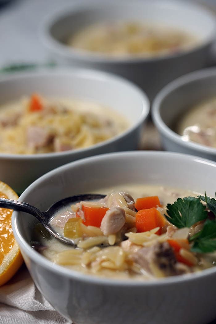 A bowlful of Lemon Chicken Orzo Soup with a spoon getting ready to dunk a big spoonful out to enjoy!