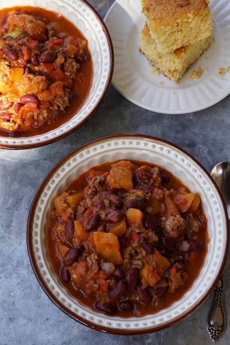 Two bowls of chili with a couple servings of cornbread on the side.