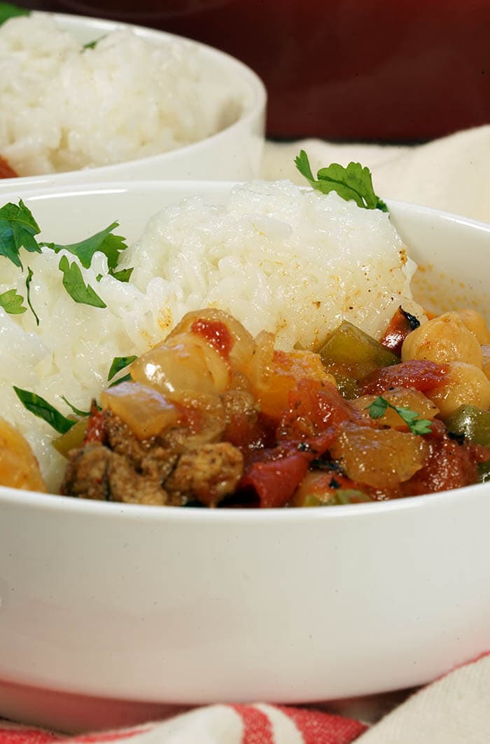 A white bowl filled with Moroccan Chicken Stew served with a side of rice. The meal is garnished with minced cilantro.