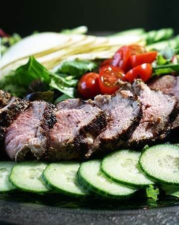 Grilled pork tenderloin salad with vegetables on silver platter.