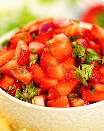 Strawberry salsa in a white bowl surrounded by chips and fresh strawberries