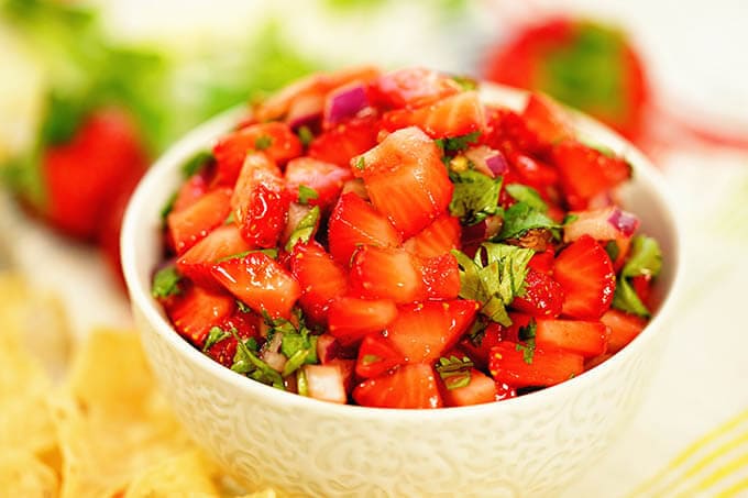 Strawberry salsa Recipe piled in a white bowl surrounded by chips and fresh strawberries