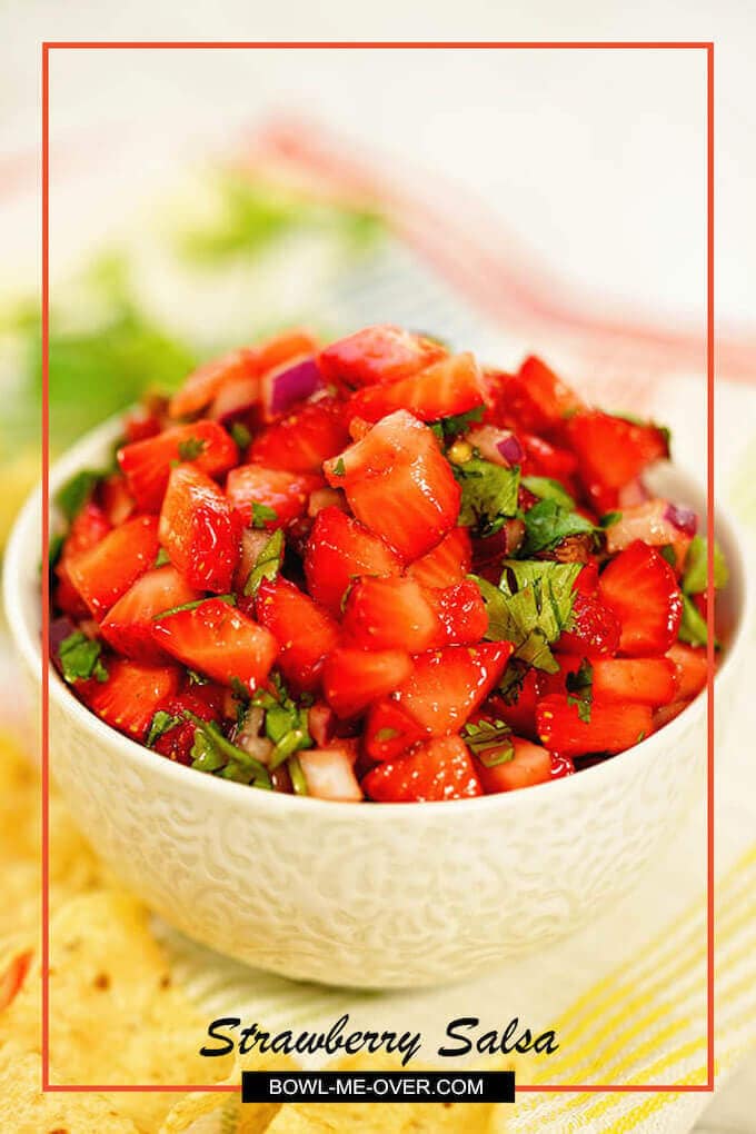 A white bowl filled iwith strawberry salsa surrounded by chips