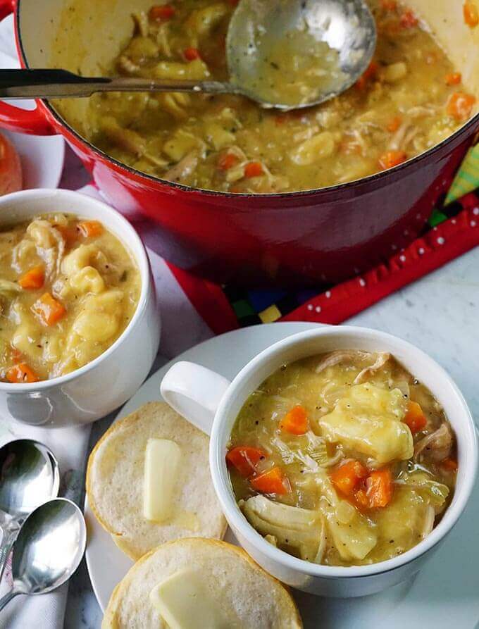 Chicken and Dumpling Soup in red pot with ladle and two bowls of soup