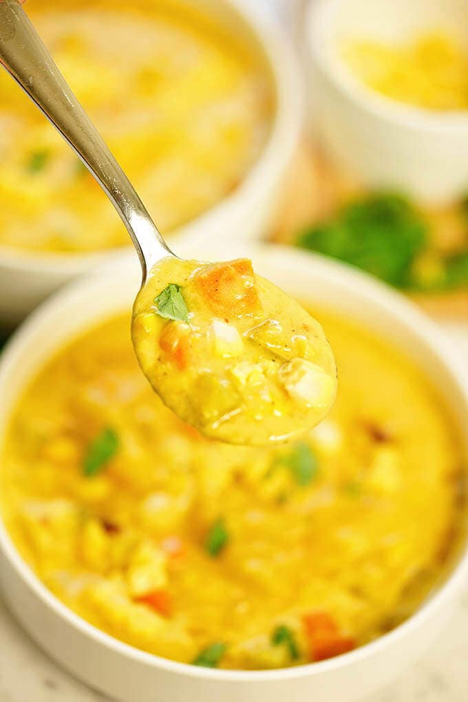 A spoonful of vegetarian corn chowder with two white bowls of chowder in the background.