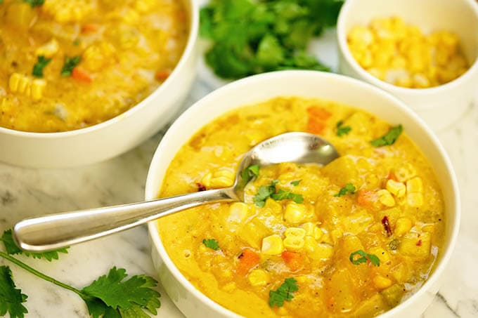 Bowls of corn chowder in white bowls with a handful of cilantro in the background.