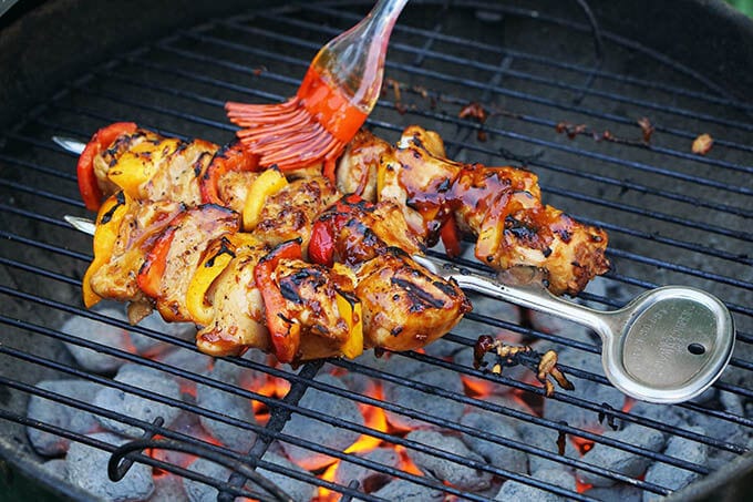BBQ Chicken skewers on hot coal grill being basted with sauce.