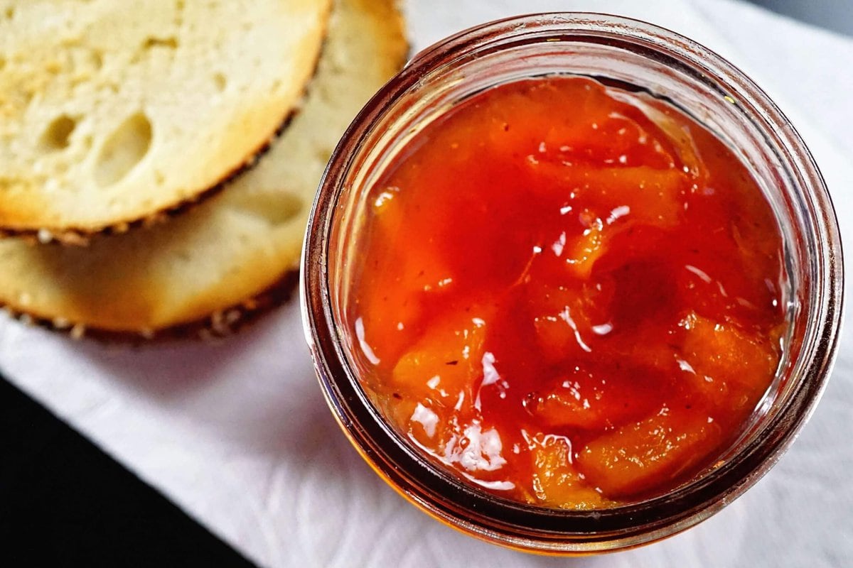 Peach Jam Recipe in a mason jar surrounded by toasted bagels