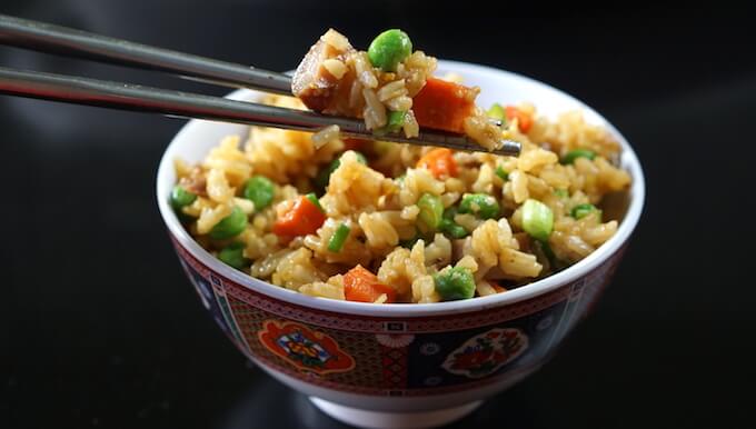 Chopsticks holding fried rice with a bowl of rice 