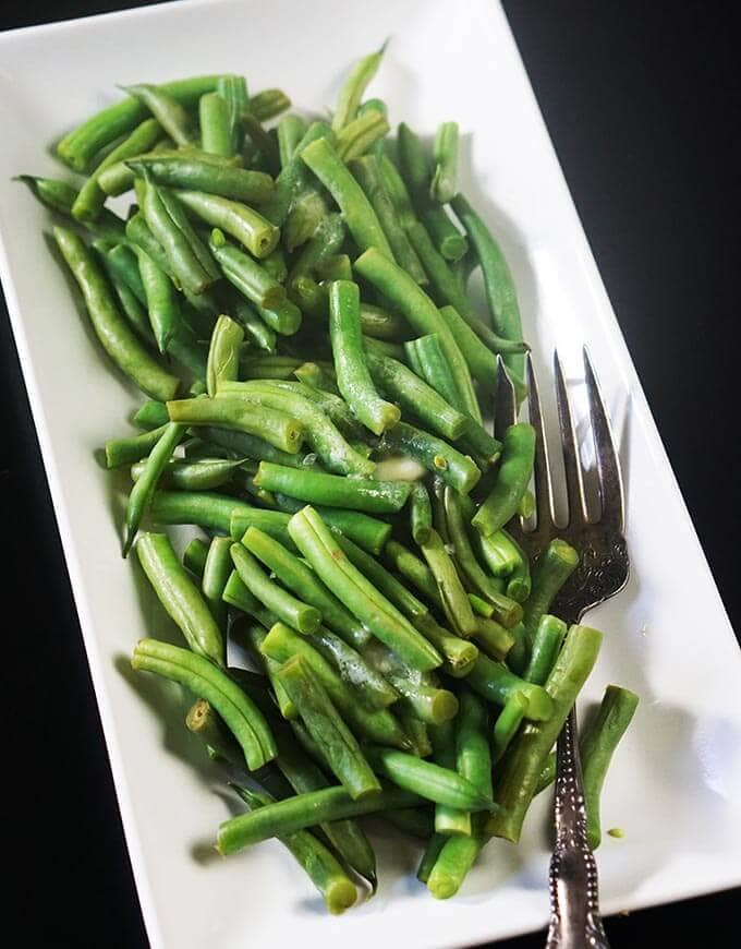 Steamed Green beans on a white platter sitting on a black tablecloth.