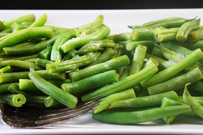 Steamed green beans on a white platter sitting on a black table.