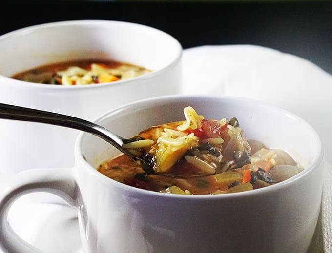 A white bowl filled with soup. There's a spoon serving up a healthy meal of vegetable orzo soup.