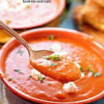 Two bowls filled with tomato bisque topped with goat cheese