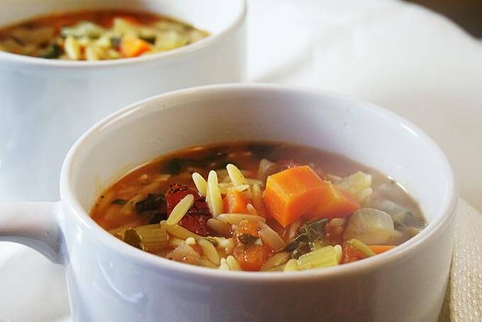 Two white bowls fill with vegetable orzo soup sitting on a white table cloth.