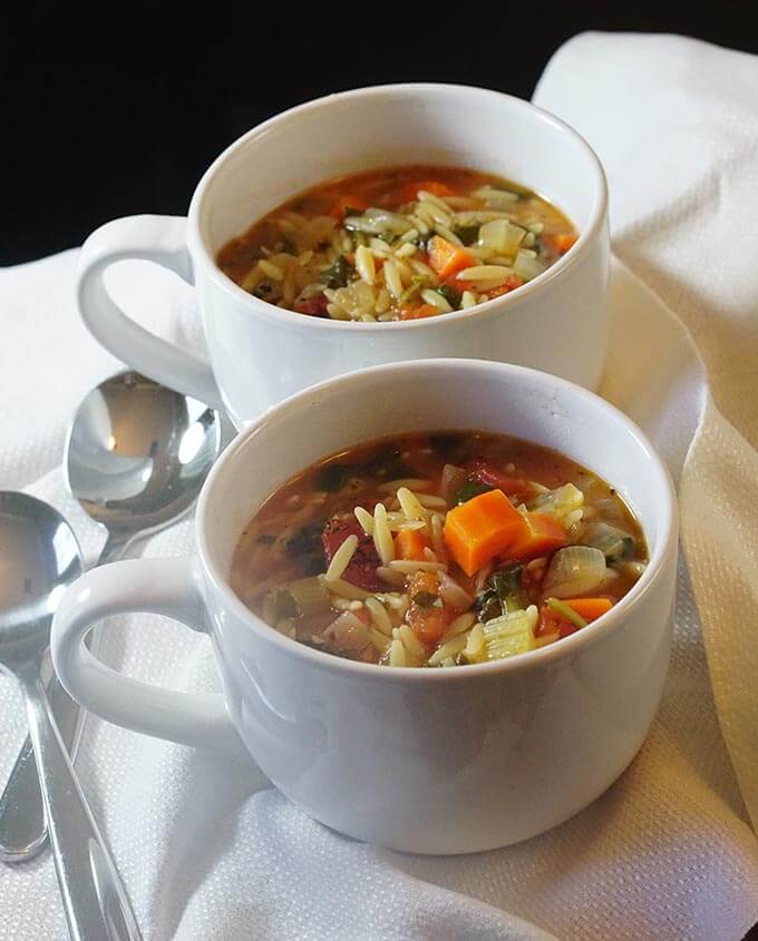 White bowls filled with orzo veggie soup on with spoons.