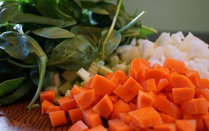 Chopped spinach, carrots and onions on a wooden cutting board.