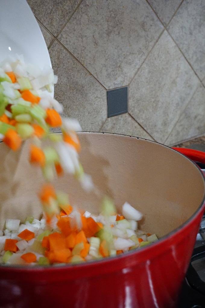 Onions, carrots and celery being poured into a red soup pot.