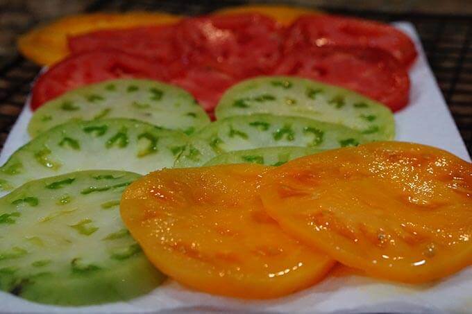 A platter of sliced tomatoes. There are several different varieties, orange, red and green tomatoes.