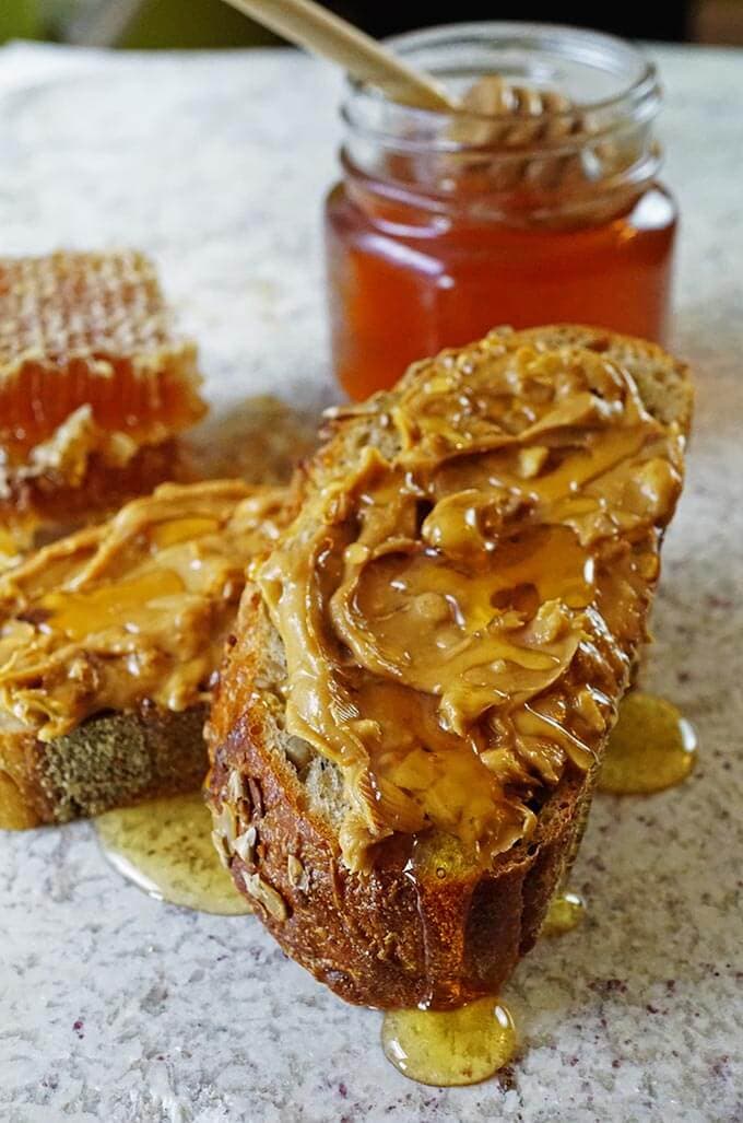 Peanut butter and honey sandwich on white platter with jar of honey.