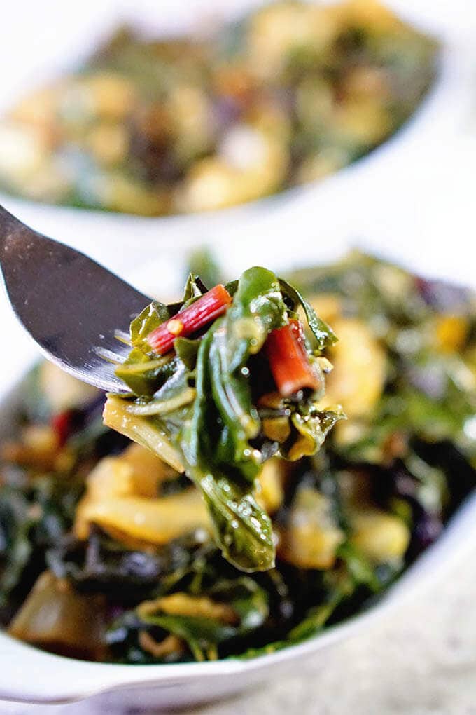 How to make Swiss chard - a fork full of the vegetables with white bowls in the background filled with cooked chard.