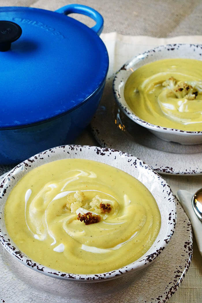 Two white bowls filled with Creamy Soup along with blue pot.