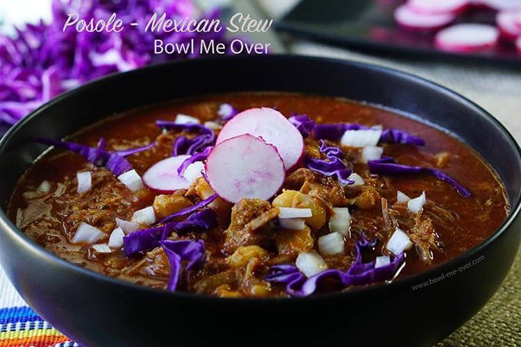 A bowl dishes up with an authentic posole recipe. The stew is topped with sliced radishes, onions and purple cabbage.