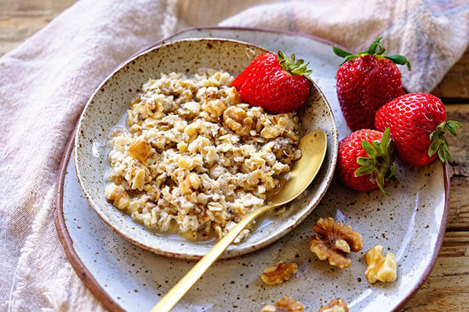 A bowl over overnight oats, sprinkled with walnuts and sliced strawberries.