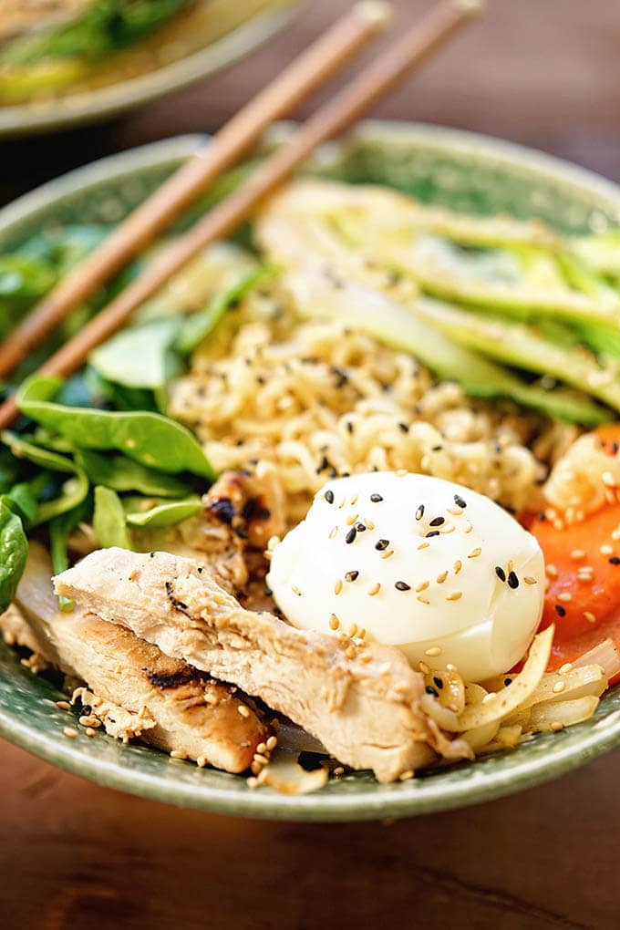 Green bowl filled with Ramen Noodles, chicken, bok choy, carrots and spinach topped with toasted sesame seeds