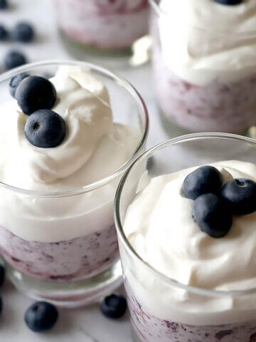 Blueberry parfaits in dish topped with whipped cream and frees blueberries.