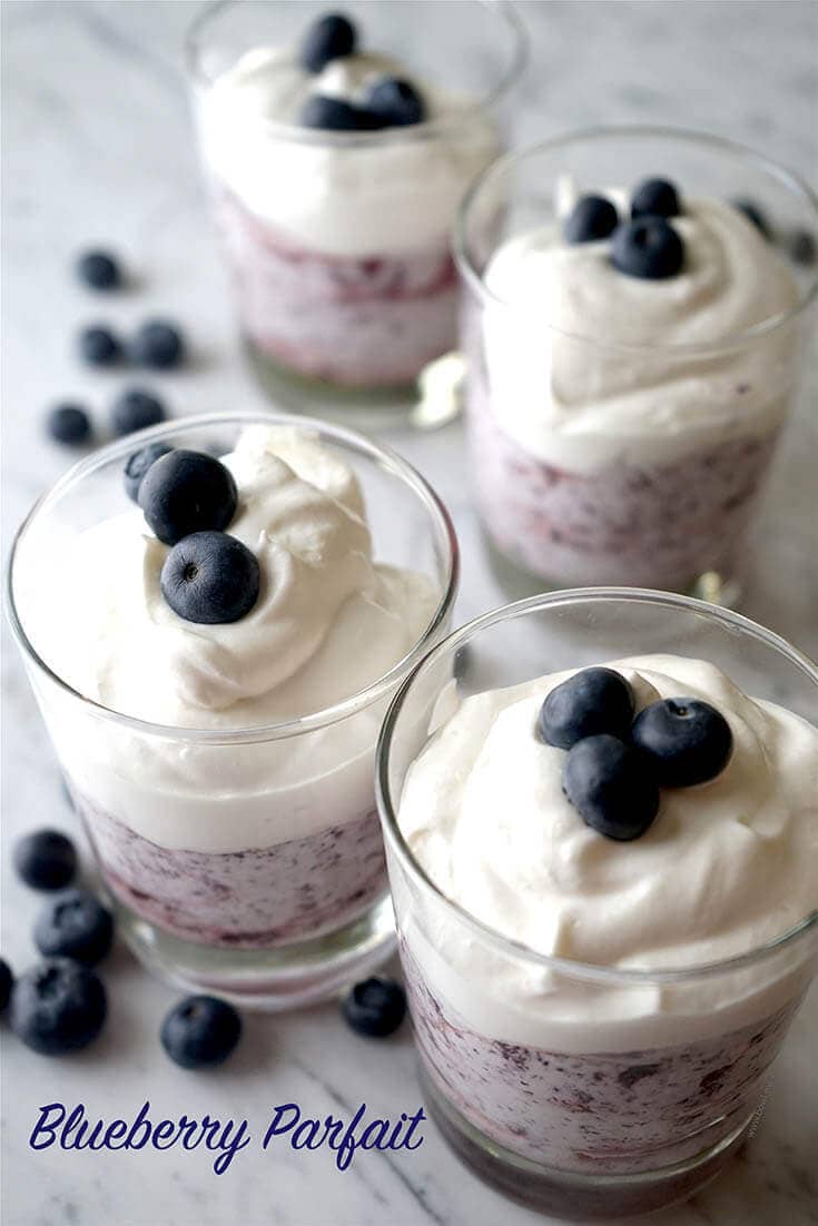 Four parfait glasses filled with blueberry mousse, topped with a dollop of homemade whip cream. Each glass is garnished with blueberries!
