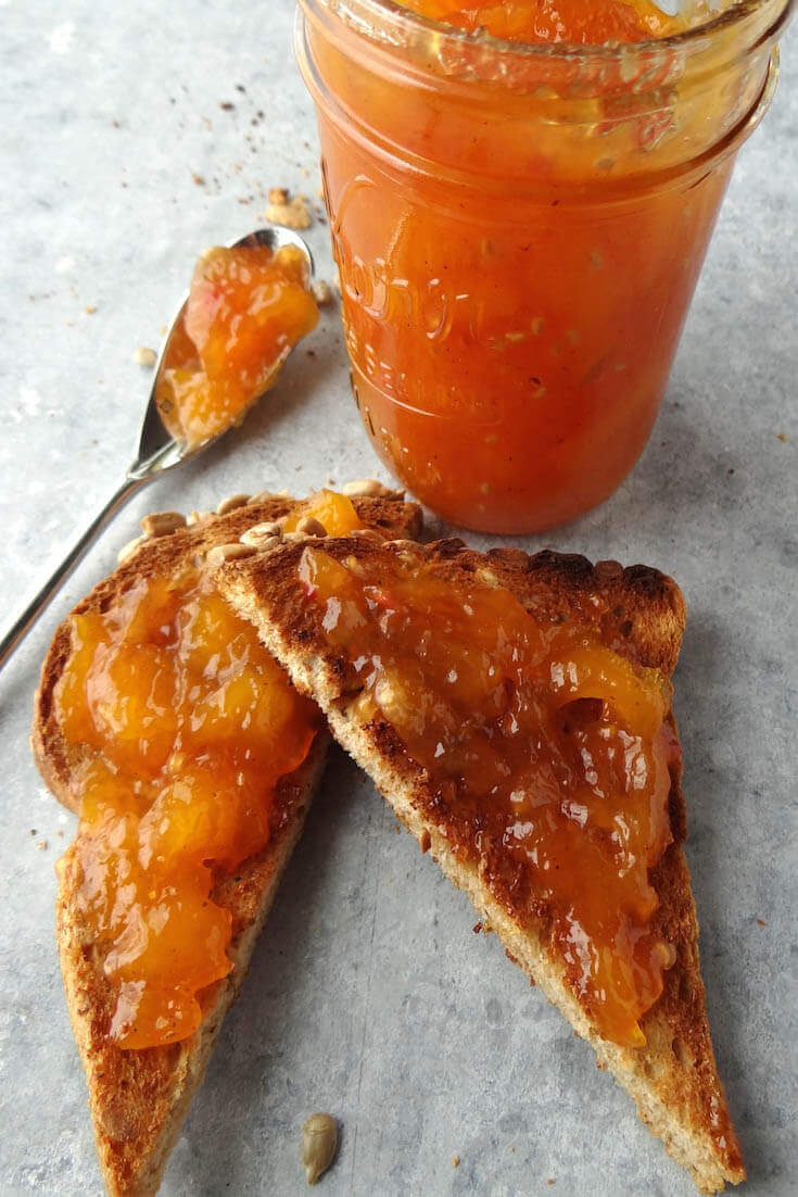 Slices of toast smeared with homemade mango jam. There's a jar in the background along with a spoon filled with more jam to spread.