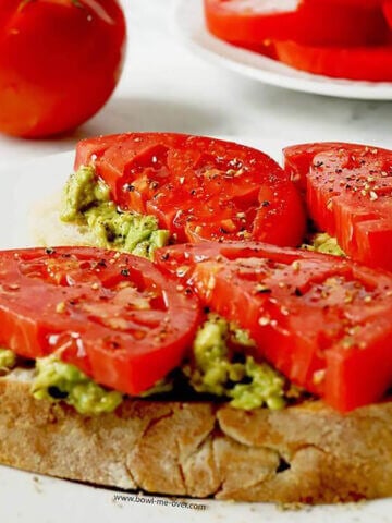 Tomato Avocado Sandwich on plate with sliced tomatoes in the background.